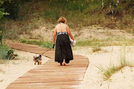 A woman on vacation walks along a wooden bridge to the beach by the sea. The sandy beach has a wooden path to the sea. Femaleの写真素材