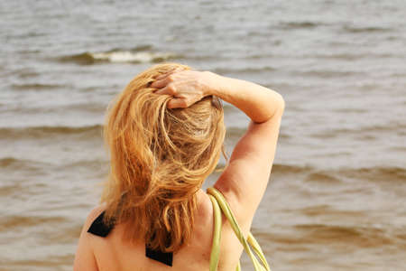 Young woman in bikini on the beach with her hand dissolves her hair. A tanned woman on vacation is resting at the sea. Beautiful female hair on the background of the sea.の写真素材