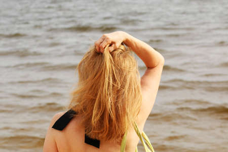 Young woman in bikini on the beach with her hand dissolves her hair. A tanned woman on vacation is resting at the sea. Beautiful female hair on the background of the sea.の写真素材