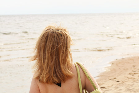Young woman in bikini on the beach with her hand dissolves her hair. A tanned woman on vacation is resting at the sea. Beautiful female hair on the background of the sea.の写真素材