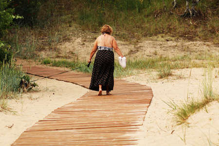A woman on vacation walks along a wooden bridge to the beach by the sea. The sandy beach has a wooden path to the sea. Femaleの写真素材