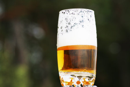 Golden foamy drink in a transparent glass on the background of the sea and the beach.. Beer with foam in a glass with a beautiful background.の写真素材