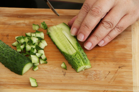 A woman cuts a cucumber for salad with a knife. A woman's hand holds a knife in her hand, a cucumber and a salad lie on the sotol.の写真素材