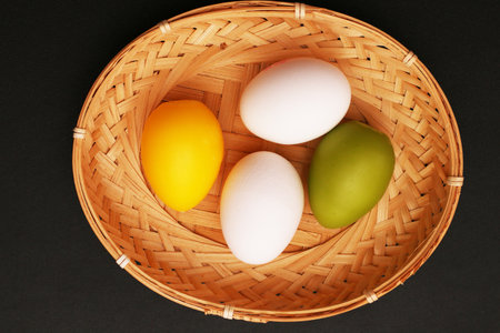 Painted eggs in a wicker basket for Easter. Colored eggs close-up on a black background.