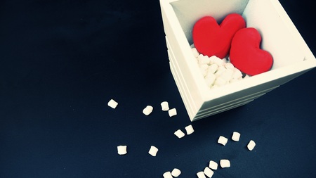 side view of red heart shape made by clay in white vase and marshmallows on shiny blackboard,...