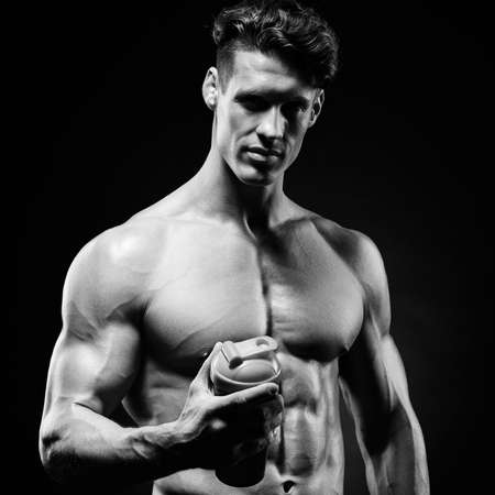 Man bodybuilder posing on gray background Man is holding a shaker for drinks. Man drinking a protein shake, water, amino acids from the shaker. Sports, sports nutrition, food additive.の写真素材