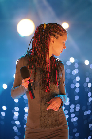 young beautiful girl with a microphone in hand, singing on stage in the rays of lightの写真素材