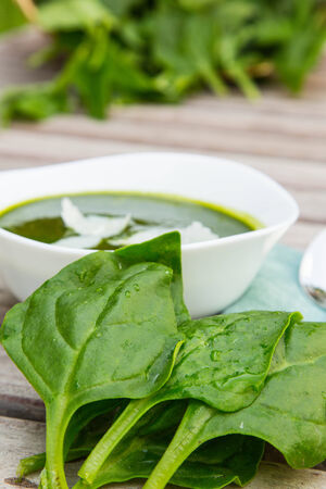 Fresh leaves of spinash with some water drops on it. Spinach cream soup in the backgroundの写真素材