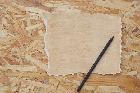 A sheet of distressed carton paper and a black pencil on the wooden surface. Free space for a text