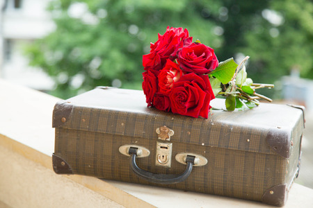 Vintage suitcase and a bunch of red roses on the balcony wall with green backgroundの写真素材