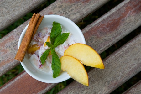 Homemade peach yogurt in a white dish on the old wooden surface. Decorated with two slices of fresh peach and fresh peppermint leaves and cinnamon stick. Top view.の写真素材