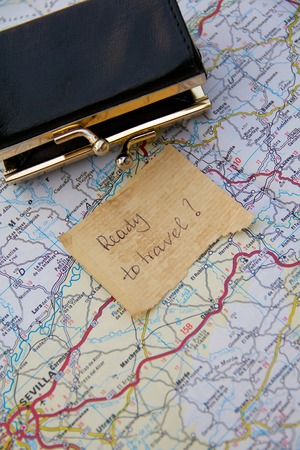 Message left on the road map close to the small opened and empty wallet:Ready to travel?