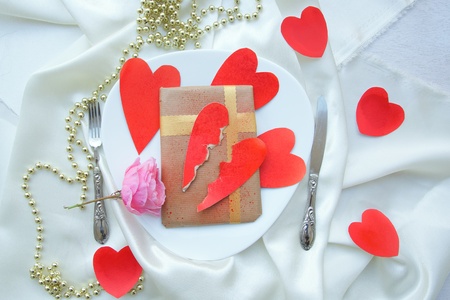 Romantic Valentines Day dinner for a ladykiller: white plate full of red hearts, pink rose,valentines day gift,broken heart. The plate is place on a white fabric. Fork,knife,red hearts,golden perl chain on a white surfaceの写真素材