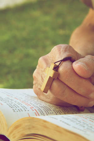 A hand of senior woman with wooden cross on a franciscan prayer book. Vintage image style. Free space for a textの写真素材