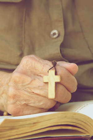 A hand of senior woman with wooden cross on a franciscan prayer book. Vintage image style.の写真素材