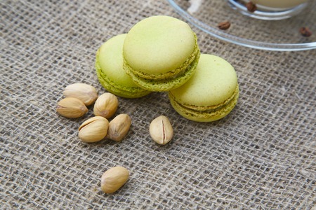 Pistachios macaroons on the sackcloth. A cup of cappuccino in the background.Pistachios in front viewの写真素材