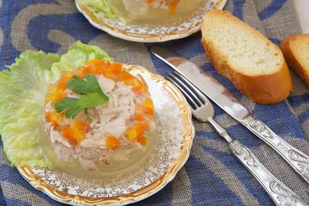 Jellied minced chicken with carrots,parsley,garlic cloves,pepper. Bread,fork and a knife in the backgroundの写真素材