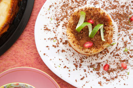 A piece of cake with chocolate chips,lemon skin and pomegranate grains on a white plate. Top view