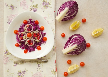 Vitamin salad in a triangular white plate: purple cabbage with cherry tomatoes, onion,salad leaves,pomegranate grains,lemons juice and olive oil. Background. Top view.の写真素材