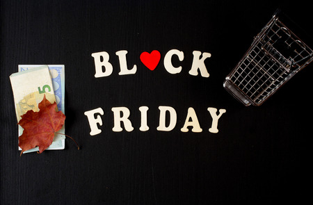 Black fridays background: wooden letter,shopping min cart,maple leaf,and money on a black wooden chalkboard.の写真素材