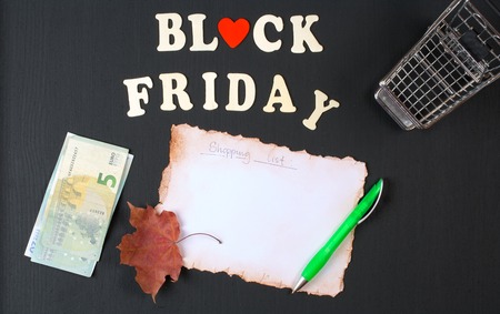 Black friday background: shopping cart, list,maple leaf,green pen,money,wooden letter on a black wooden chalkboardの写真素材