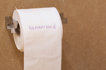 The word hemorrhoid is written on a roll of white patterned toilet paper hanging on a holder in a bathroomの写真素材
