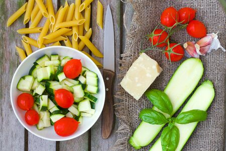Food ingredients for preparing pasta: zucchini, penne rebate,cherry tomatoes,parmesan cheese, fresh basil leaves, garlic on an old wooden surface. Overhead perspectiveの写真素材