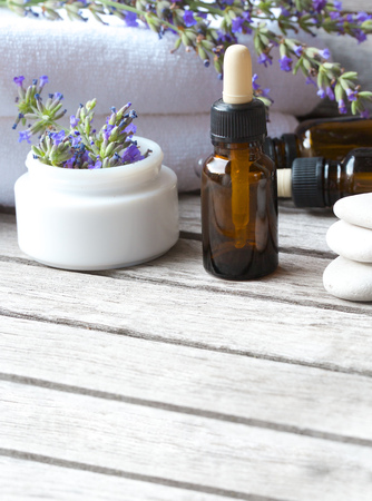 A dropper bottle with lavender essential oil on a old wooden surface. Lavender twig and white towels in the background.の写真素材