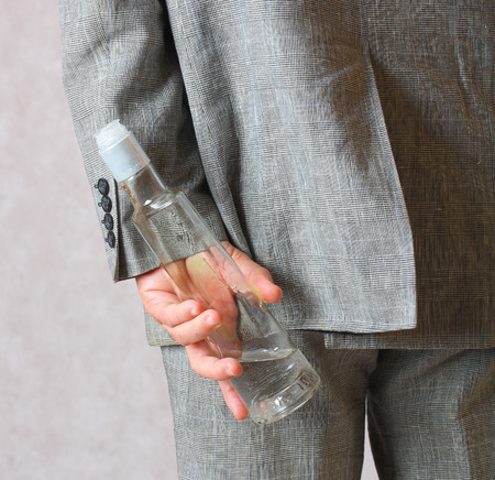 A man dressed in a classical costume hides a bottle of alcohol behind the back.Closeupの写真素材