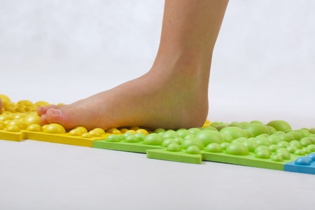 The feet of small children on a orthopaedic mat. White background. Free space for a text.の写真素材