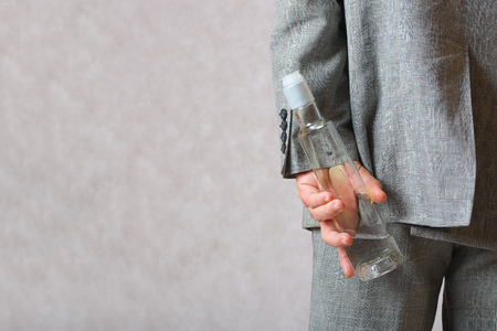 A man dressed in a classical costume hides a bottle of alcohol behind the back.Closeupの写真素材