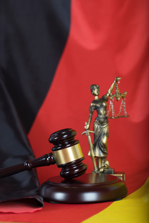Judge's gavel. Closeup. Flag of Germany and statue of Themis in the background.の写真素材