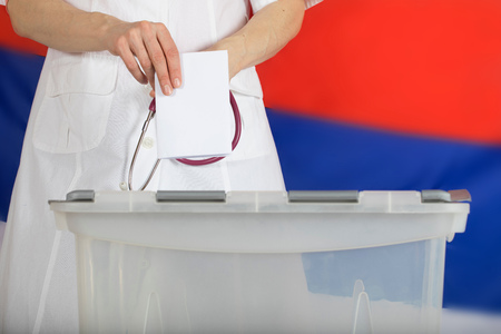 Doctor's hand casts ballot paper in the ballot box. Russian flag in the background.の写真素材
