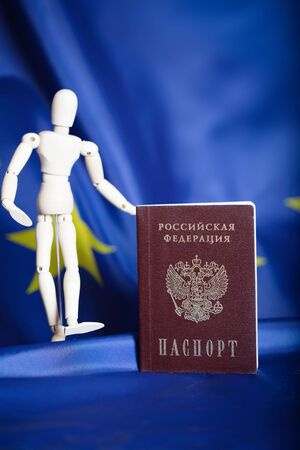 Russian pass and wooden dummy figurine on Russian and European flag. Translation on the pass- Russian Federation. Passport. Closeupの写真素材
