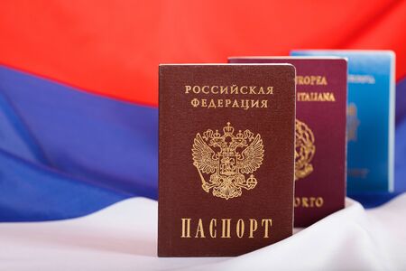 Russian pass in front of Moldovan and Italian ones. Russian flag in the background.Translation on the pass- Russian Federation. Passport. EU. Italian Republic. Passportの写真素材