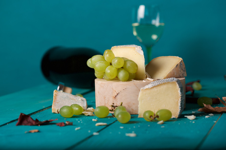 Cheese slices, white grapes, knife, glass and a bottle  of white wine on a wooden surface. Closeupの写真素材