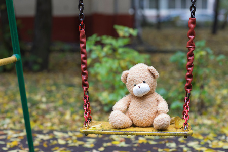 Brown plush teddy bear on a yellow colourful swing.の写真素材
