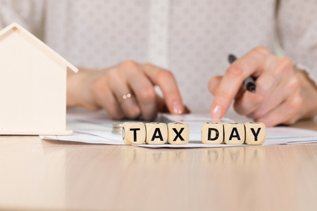Word TAX DAY composed of wooden letters. Female hand with a pen in the background. Closeupの写真素材
