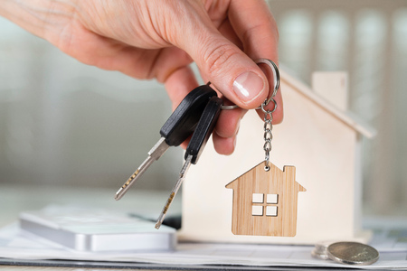 Female keeps house key on a key hanger in front of a wooden house. Closeup