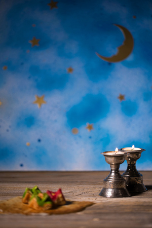 Candles on a wooden surface. Arabic sweets and night blue sky with crescent moon in the background.の写真素材