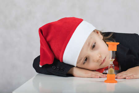 Boy of four years in Santa's hat observes sand watch. Closeupの写真素材