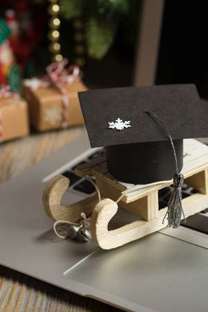 Small wooden sleigh with graduate cap on it placed on a laptop. Closeup