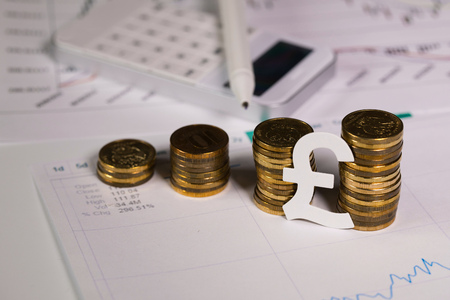 Cutout of British pound at stacks of coins. Calculator with a pen in the background