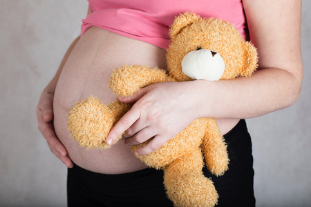 Young pregnant between 30 and 35 years old woman keeps plush brown teddy bear. Closeupの写真素材