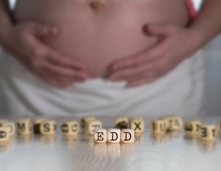 Abbreviation EDD composed of wooden letters - Estimated Due Date. Pregnant woman in the backgroundの写真素材