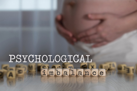 Words PSYCHOLOGICAL IMBALANCE composed of wooden letters. Pregnant woman in the backgroundの写真素材