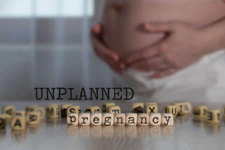 Words UNPLANNED PREGNANCY composed of wooden letters. Pregnant woman in the backgroundの写真素材