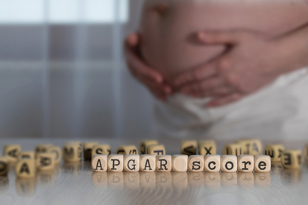 Words APGAR SCORE composed of wooden letters. Pregnant woman in the backgroundの写真素材