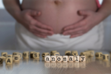 Word ANOMALY  composed of wooden letters. Pregnant woman in the backgroundの写真素材