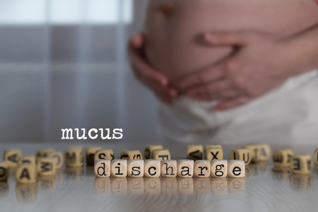 Words MUCUS DISCHARGE composed of wooden letters. Pregnant woman in the backgroundの写真素材